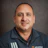 Professional headshot of man in navy Advantive branded jacket against gray background Headshot
