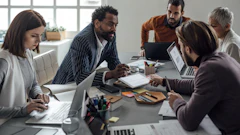 Diverse team collaborating during business meeting with laptops and documents at modern office table