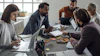Diverse team collaborating during business meeting with laptops and documents at modern office table