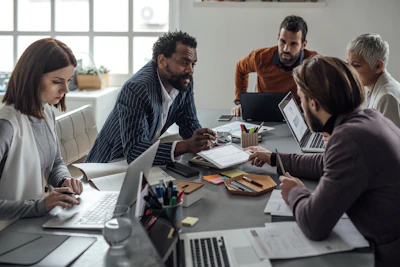 Diverse team collaborating during business meeting with laptops and documents at modern office table