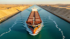 Large red and black cargo ship navigating through the Suez Canal with sandy desert banks on both sides