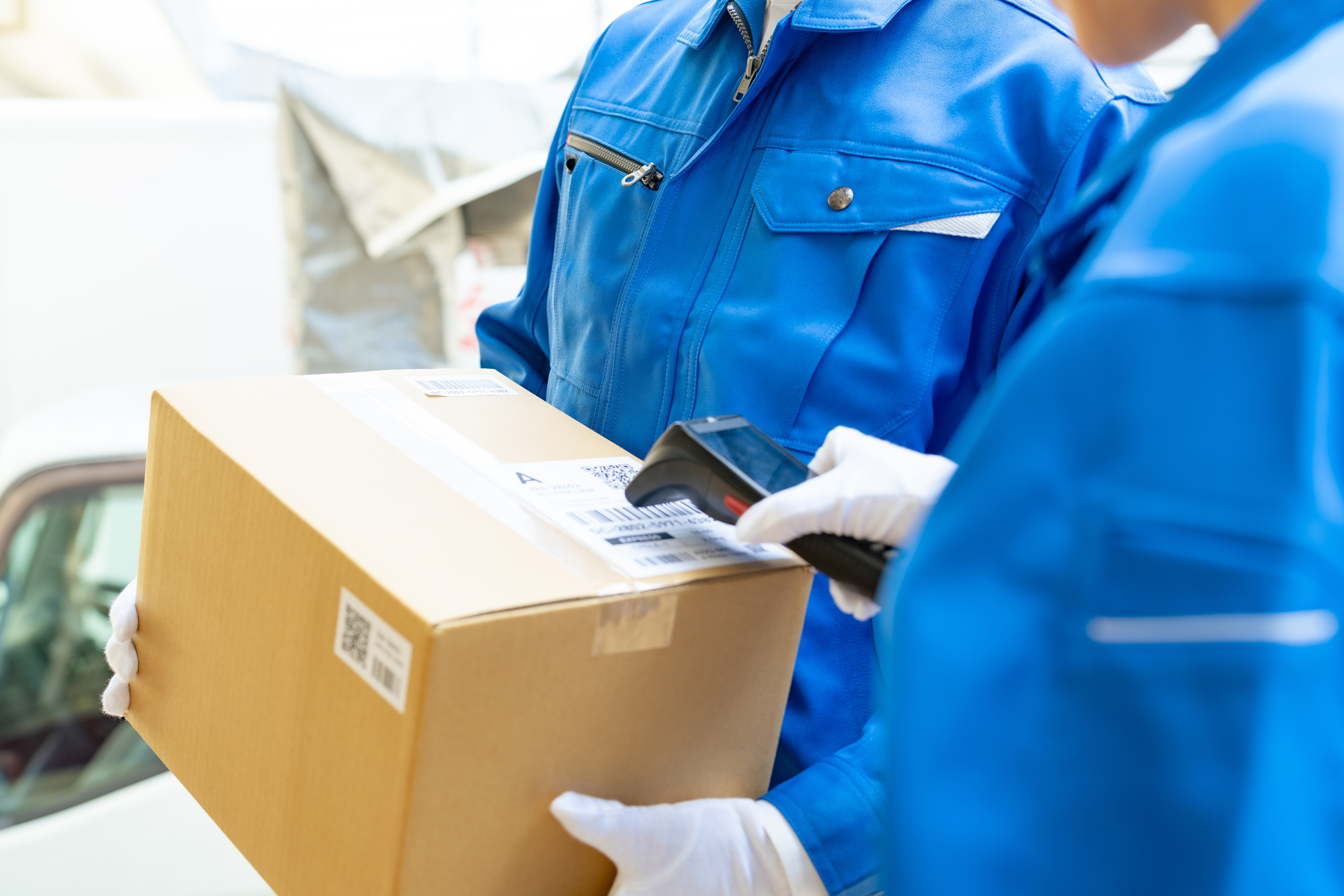 Delivery worker in blue uniform scanning a cardboard package with a handheld barcode scanner