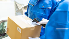 Delivery worker in blue uniform scanning a cardboard package with a handheld barcode scanner