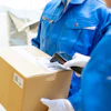 Delivery worker in blue uniform scanning a cardboard package with a handheld barcode scanner