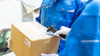 Delivery worker in blue uniform scanning a cardboard package with a handheld barcode scanner