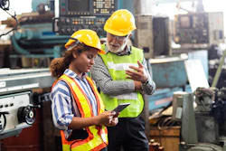 Two industrial workers in safety gear review information on tablet in manufacturing facility