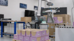 Collaborative robot arm sorting purple and brown cardboard boxes in a warehouse facility