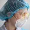 Healthcare worker wearing blue surgical cap, protective goggles, and white face mask