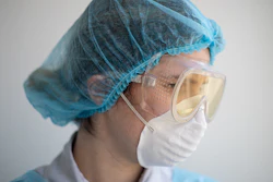 Healthcare worker wearing blue surgical cap, protective goggles, and white face mask