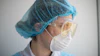 Healthcare worker wearing blue surgical cap, protective goggles, and white face mask