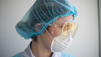 Healthcare worker wearing blue surgical cap, protective goggles, and white face mask