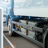 Electric truck charging at public charging station with blue banner and other vehicles in background