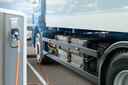 Electric truck charging at public charging station with blue banner and other vehicles in background