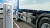 Electric truck charging at public charging station with blue banner and other vehicles in background