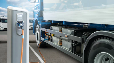 Electric truck charging at public charging station with blue banner and other vehicles in background