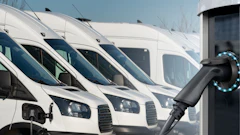 Row of white commercial vans with electric vehicle charging station in foreground