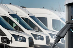 Row of white commercial vans with electric vehicle charging station in foreground