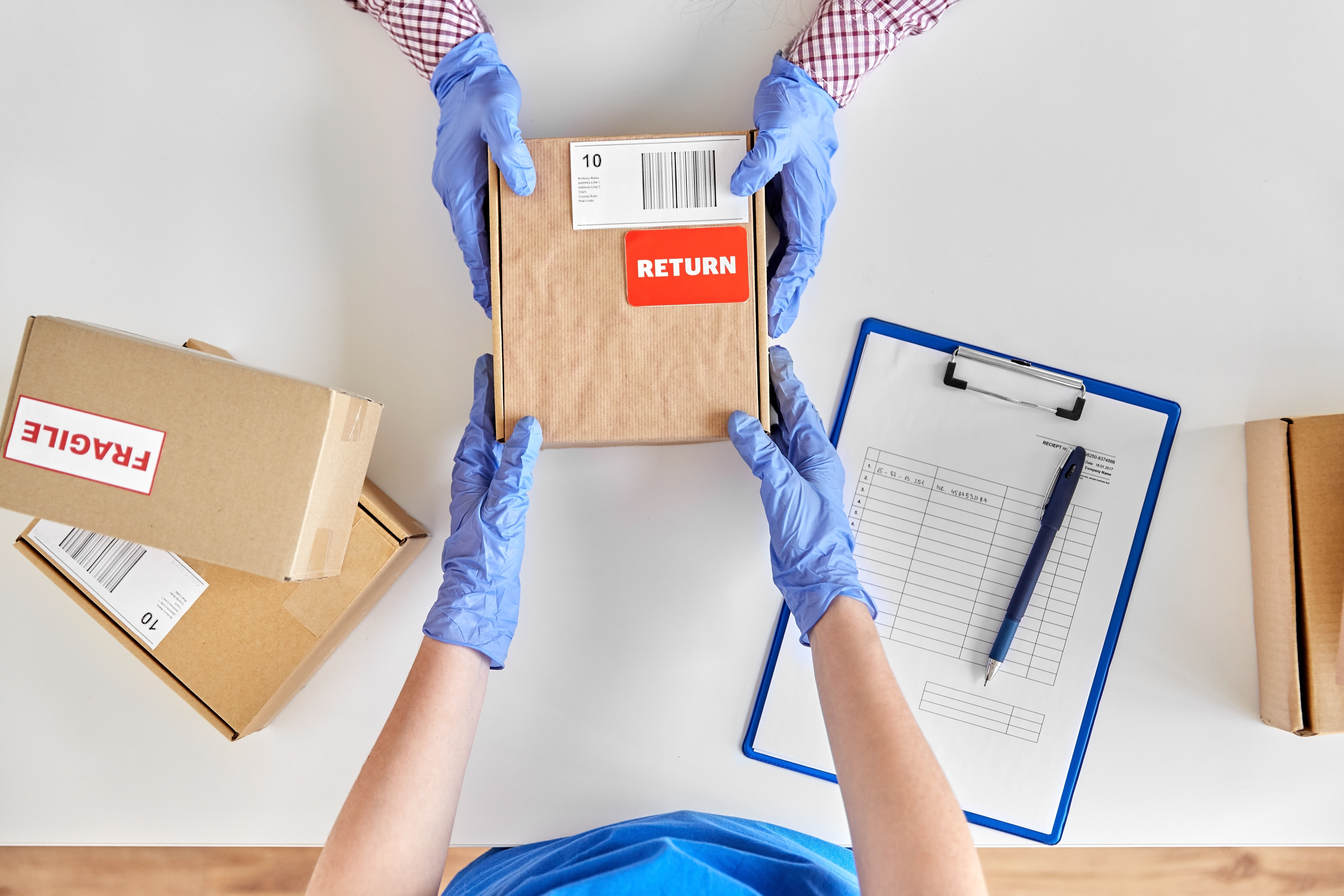 Worker in blue gloves handling cardboard boxes marked with return label and shipping documentation