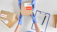 Worker in blue gloves handling cardboard boxes marked with return label and shipping documentation