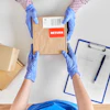 Worker in blue gloves handling cardboard boxes marked with return label and shipping documentation
