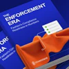 Two blue 'Enforcement Era' books displayed with orange fabric on blue background